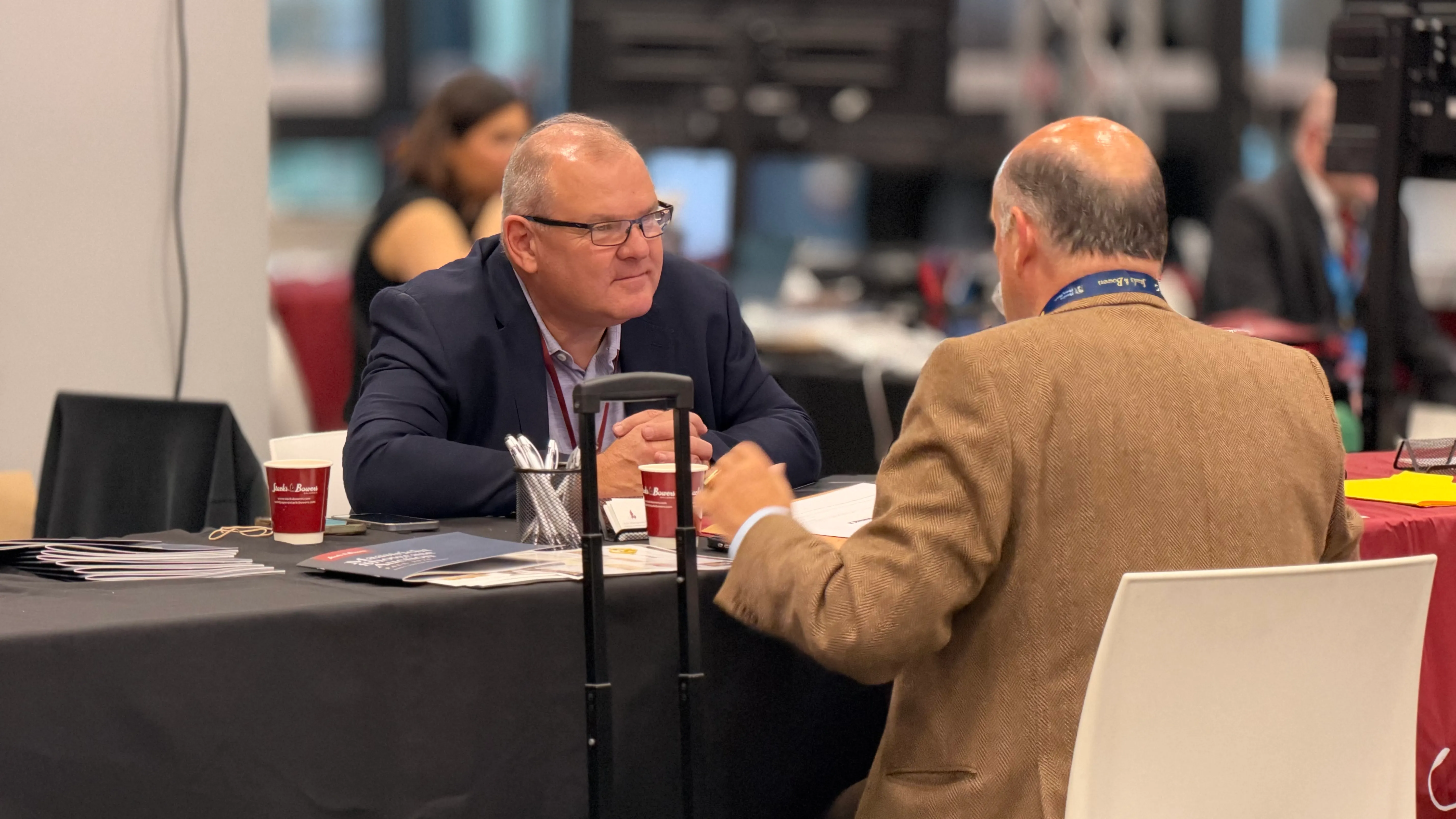 Two people in conversation at a table with Stack's Bowers cups