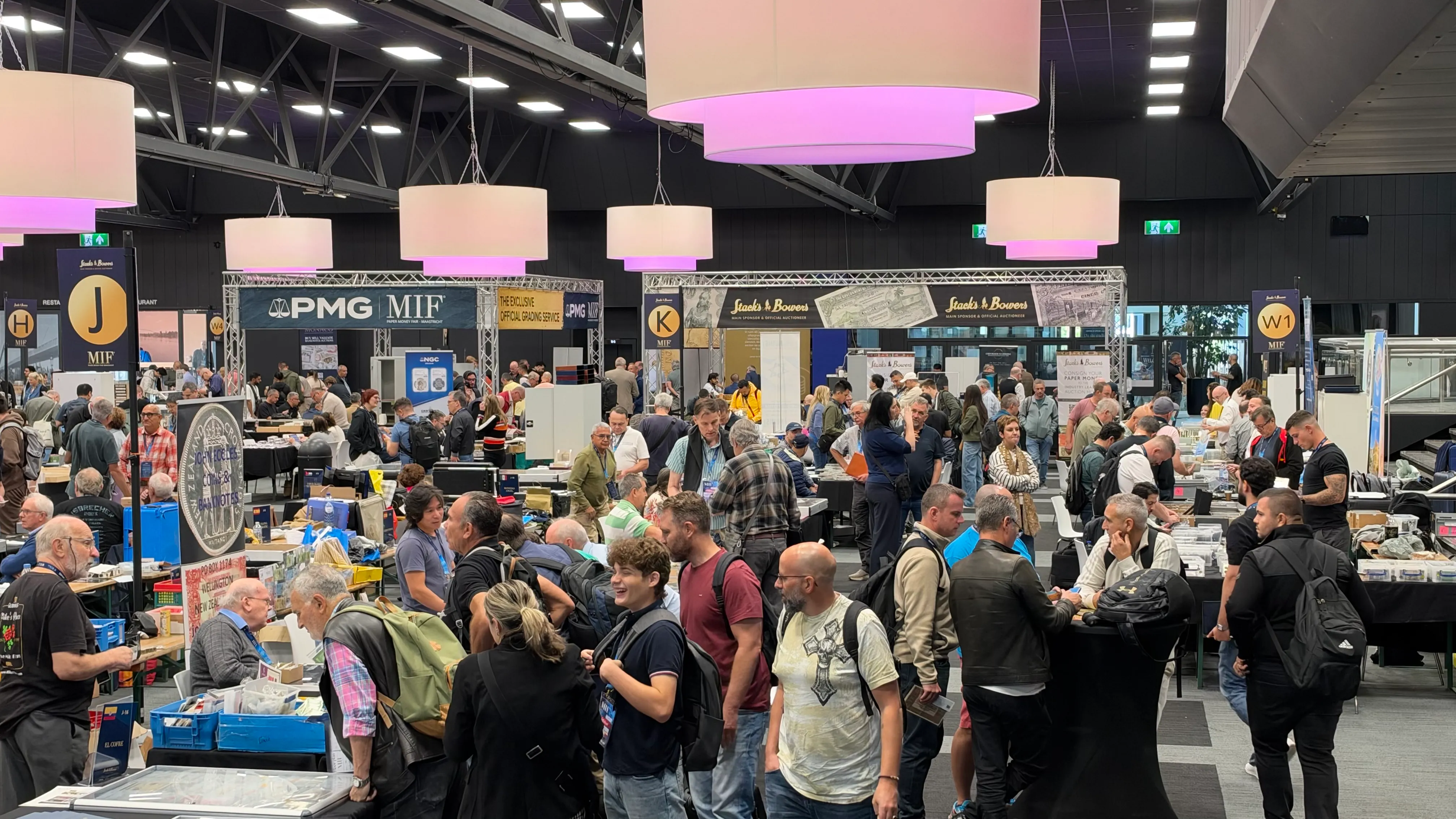 Busy exhibition hall with the PMG and Stack's Bowers stands under large pendant lamps
